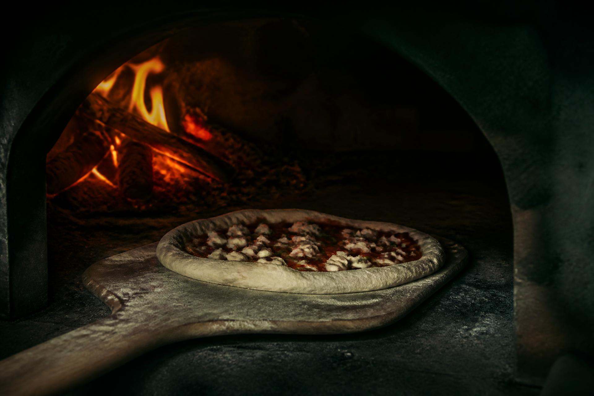 Pizza artesanal entrando en un horno de leña italiano